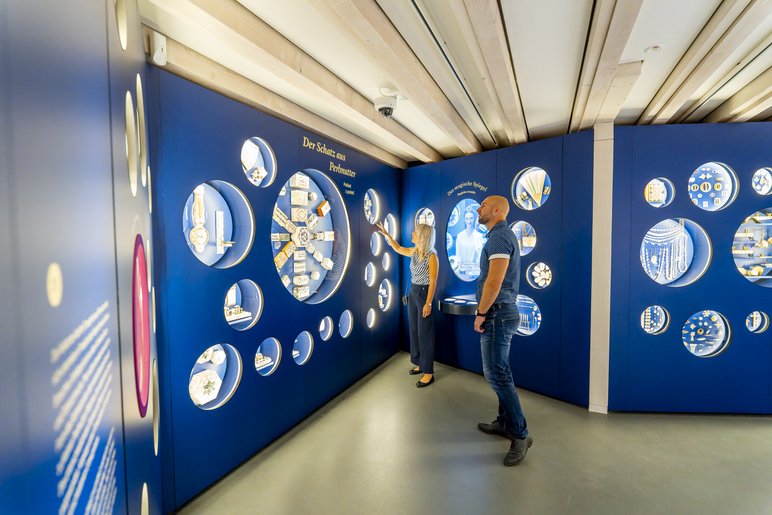 Dunkelblaue Stellwand mit eingebauten runden Vitrinen, die Objekte aus Perlmutter enthalten, vor allem Schmuckkästchen