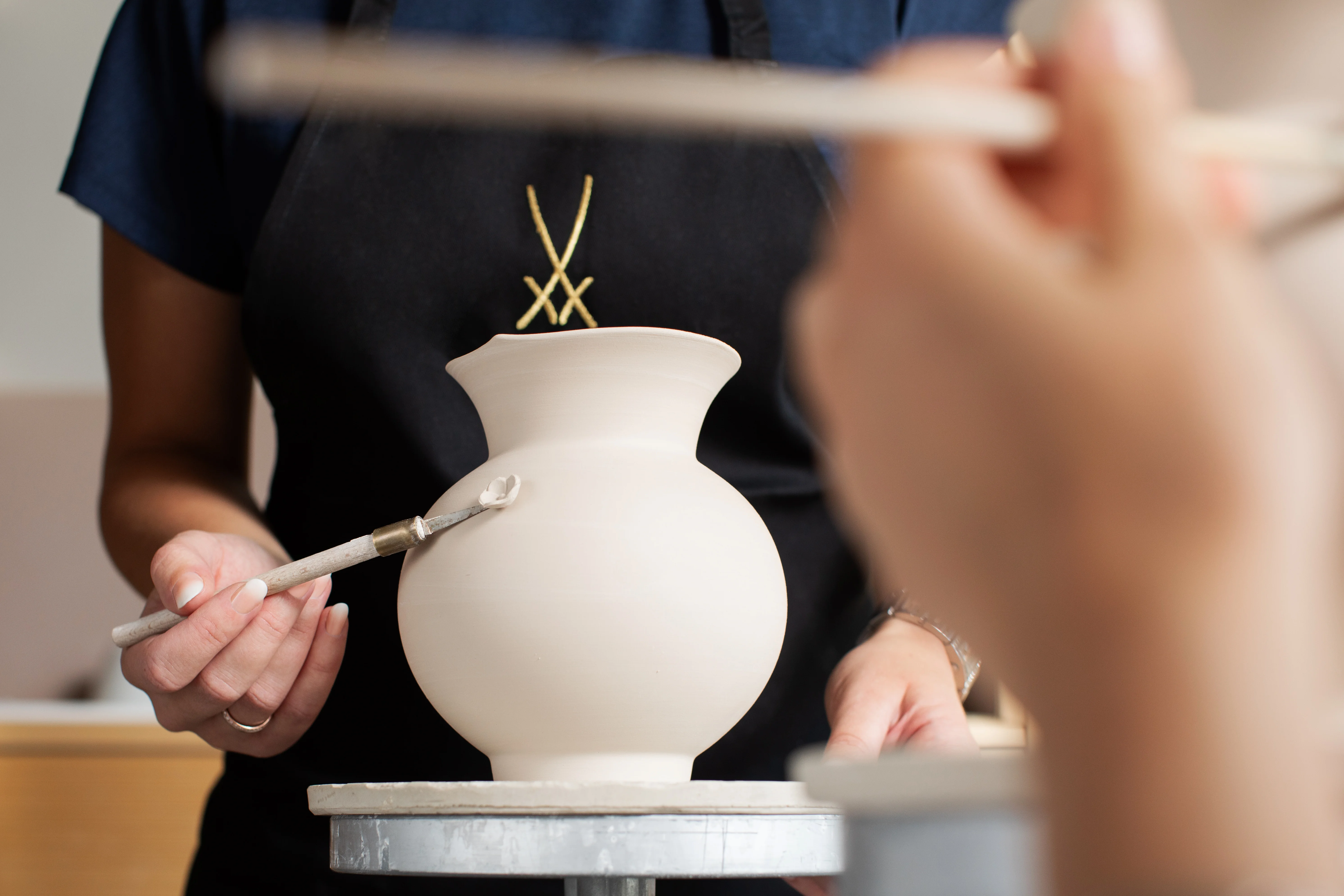 Kreativ-Workshop bei MEISSEN: Vasenform Wellenspiel Im Kreativ-Workshop bringt eine Teilnehmerin mit ruhiger Hand ein Porzellandetail an einer Vase an.