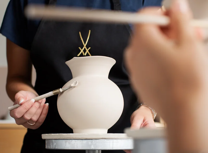Im Kreativ-Workshop bringt eine Teilnehmerin mit ruhiger Hand ein Porzellandetail an einer Vase an.