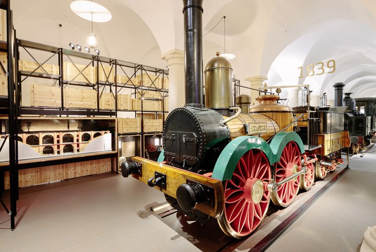 Eine historische Dampflokomotive in Schwarz- und Goldfarben mit großen roten Rädern und grünen Schutzblechen