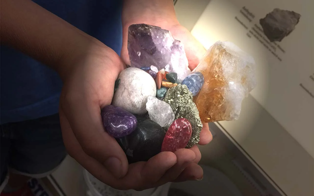 Kieselstein und Zauberstein Projekt Ein Kind hält mit beiden Händen eine Menge an bunten Steinen und Mineralien vor sich.