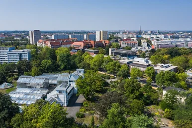 Botanischer Garten der Universität Leipzig Luftaufnahme über Gewächshäuser und viel Grün, im Hintergrund urbane Bebauung der Stadt Leipzig