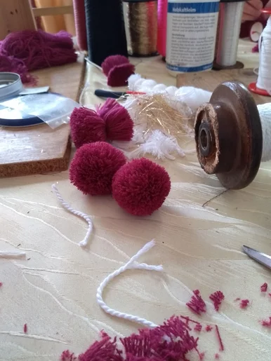 Auf einer Arbeitsfläche liegen handgefertigte Bommeln und Kordeln.