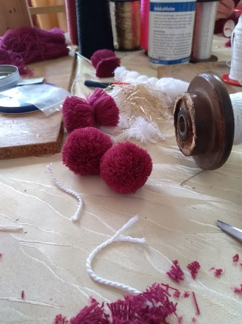 Auf einer Arbeitsfläche liegen handgefertigte Bommeln und Kordeln.