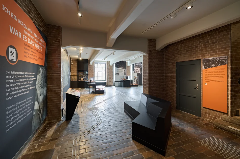 Ausstellungsbereich Sozialgeschichte Blick in die ehemalige Lohnschalterhalle der historischen Schachtanlage. An einer Wand hängt ein großer Ausstellungstext.