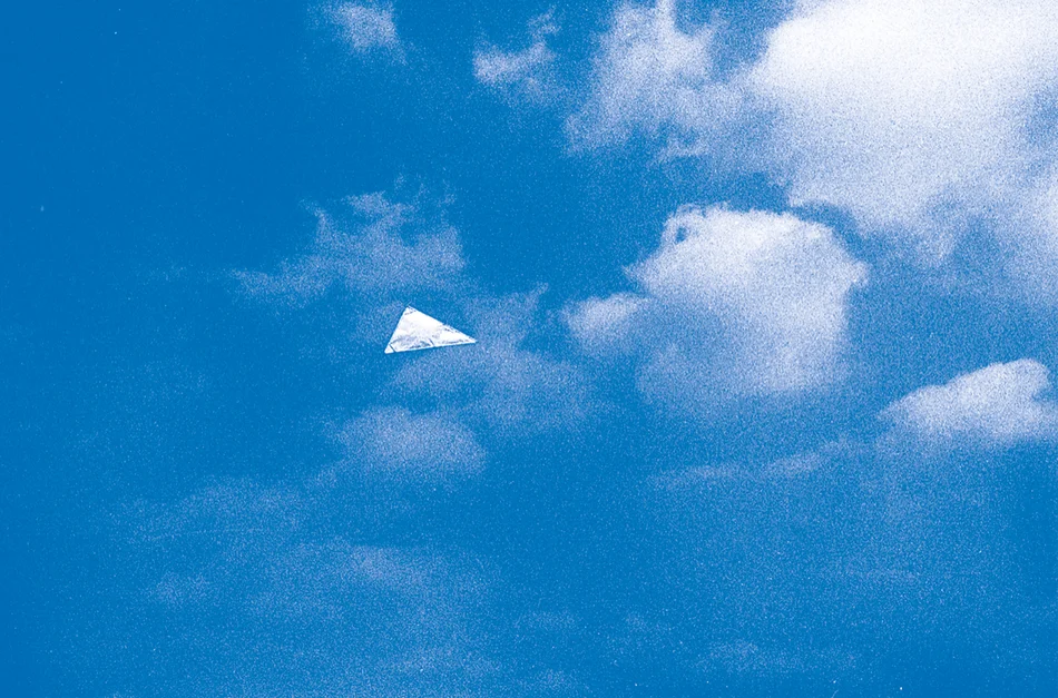 Unter einem blauen Himmel mit wenigen Wölkchen schwebt ein dreieckiges helles Objekt.