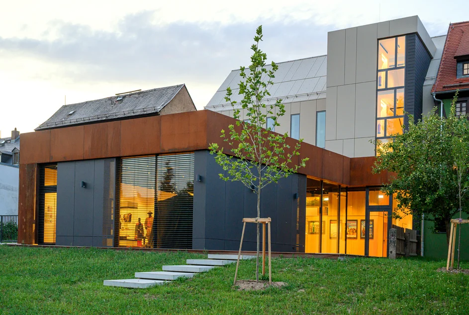 Das Foto zeigt eine Außenansicht der Rückseite des Karl-May-Hauses und des Museumsdepots bei Dämmerung. Die Fenster sind hell erleuchtet.