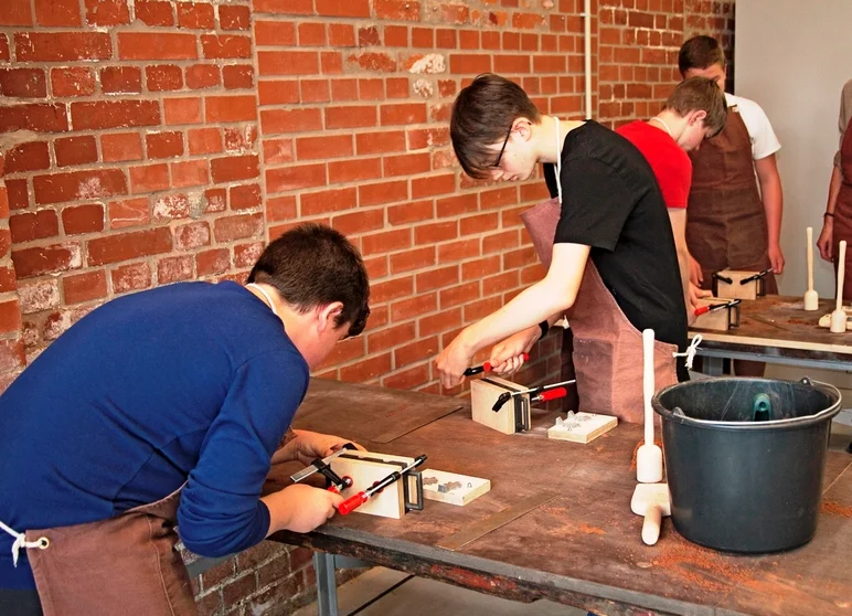 Vier Schüler stehen an Werkbänken und spannen Gussformen ein.