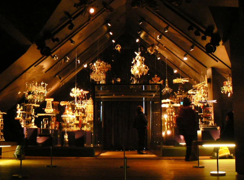 Das Foto zeigt zwei Menschen in einem beleuchteten Dachgeschossraum der Manufaktur der Träume. In dem Ausstellungsraum sind große handgeschnitzte Erzgebirgspyramiden zu sehen, und vom Spitzdach hängen handgeschnitzte Kronleuchter.