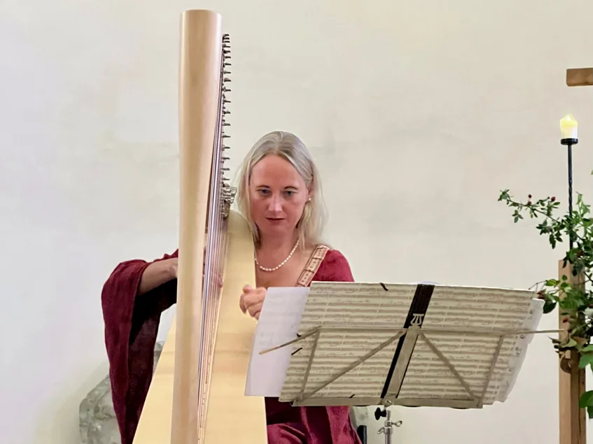 Vielsaitig. Konzertprogramm Foto einer Musikerin, die hinter einem Notenständer sitzend Harfe spielt