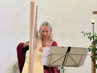 Vielsaitig. Konzertprogramm Foto einer Musikerin, die hinter einem Notenständer sitzend Harfe spielt