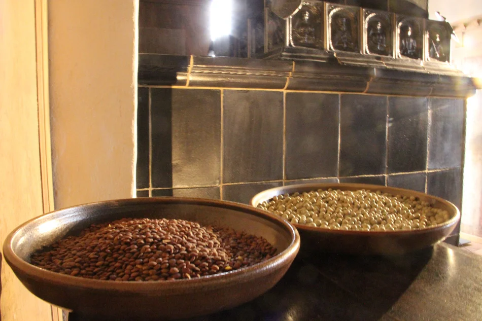 Eine Schüssel Linsen und eine Schüssel Erbsen stehen auf einer Ablage vor einem historischen Kachelofen.