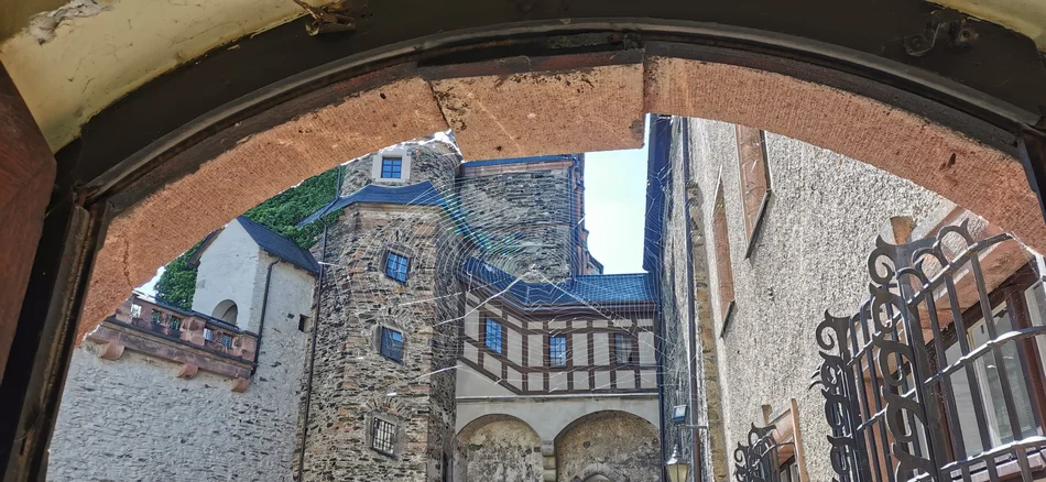 Burg Mylau, Hofansicht Blick durch einen steinernen Torbogen in den Innenhof einer mittelalterlichen Burg mit Fachwerk- und Naturstein-Elementen