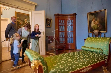 Ein Mann, eine Frau und zwei Mädchen stehen in einem historischen Gemach und schauen sich das Mobiliar und die Gemälde an den Wänden an.