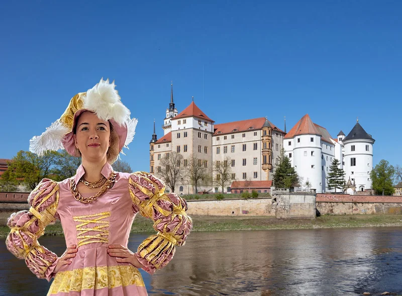 Eine als Kurfürstin Sibylle von Kleve verkleidete Frau steht vor dem an der Elbe gelegenen Schloss Hartenfels
