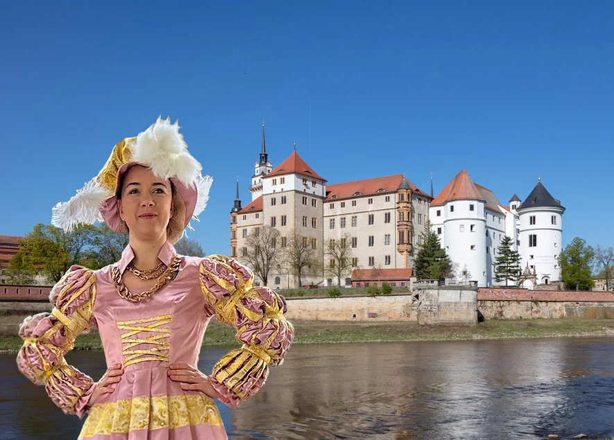 Sibylle von Kleve vor Schloss Hartenfels Eine als Kurfürstin Sibylle von Kleve verkleidete Frau steht vor dem an der Elbe gelegenen Schloss Hartenfels