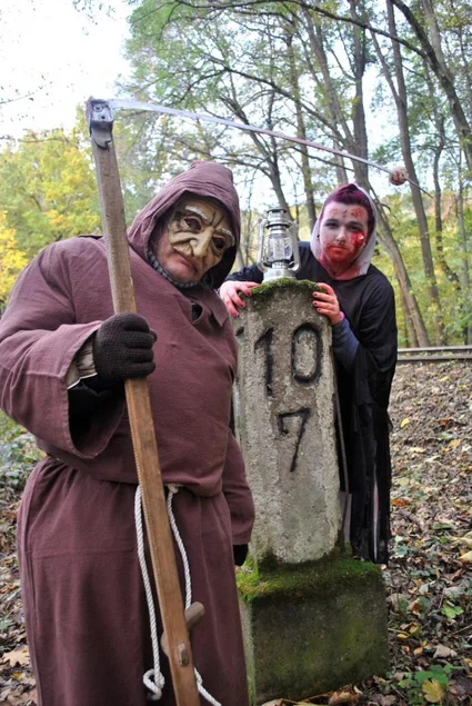 Ein als Tod mit Sense verkleideter Mann und ein mit roter Farbe beschmierter, bleicher Mann stehen nebeneinander.