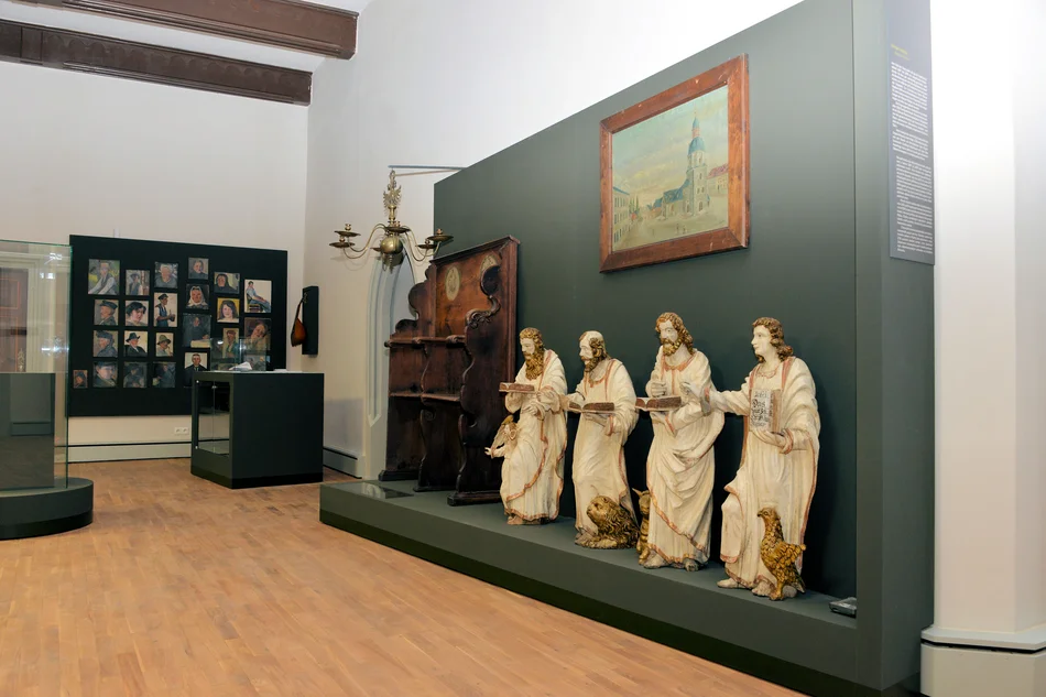 In einem Ausstellungsraum stehen vier Skulpturen sakraler Kunst, an den Wänden hängen diverse Bilder.