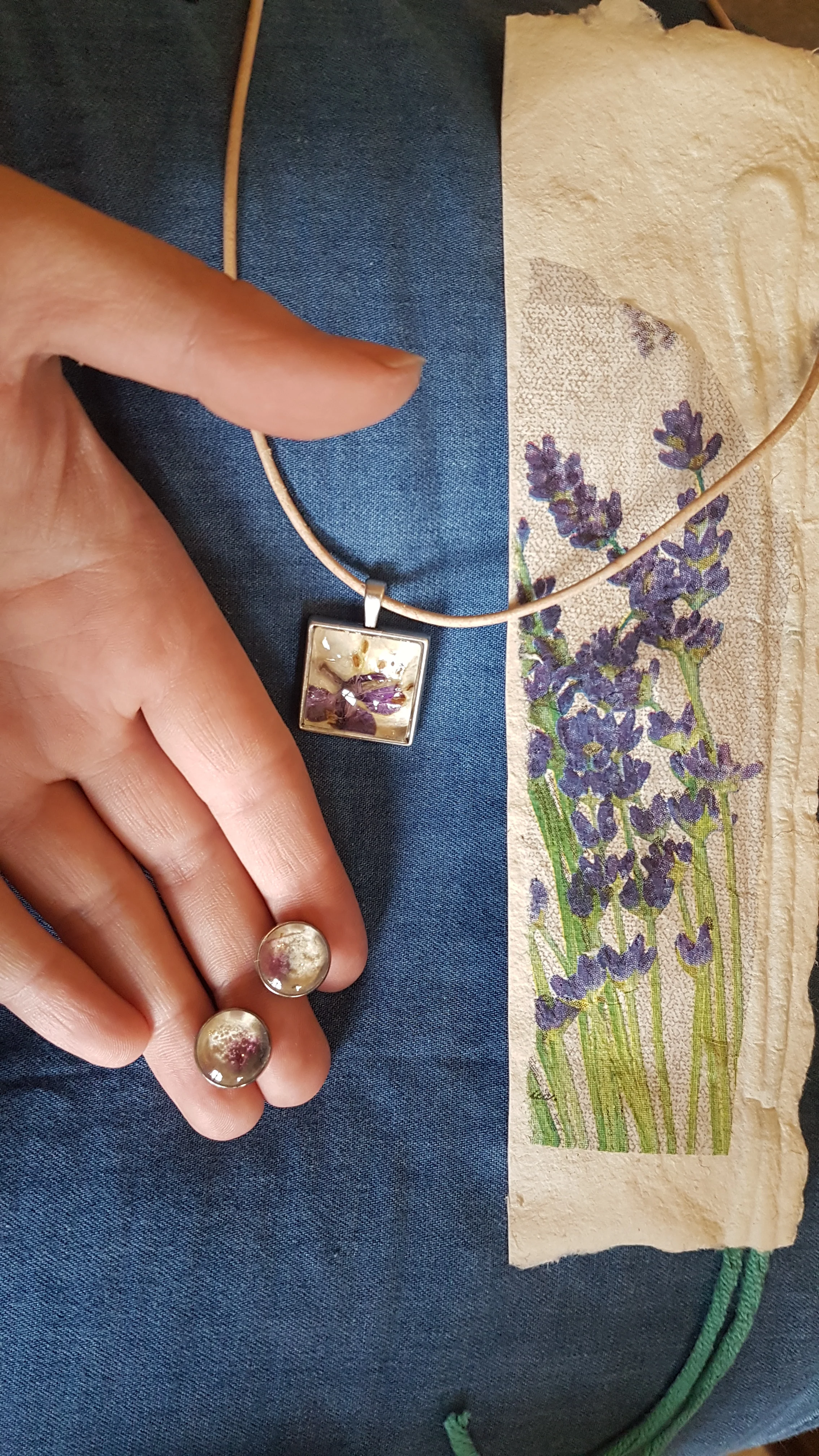 Blumiger Schmuckworkshop Eine Hand präsentiert zwei Ohrstecker und eine Kette neben frisch in Büttenpapier eingeschöpften Blüten.