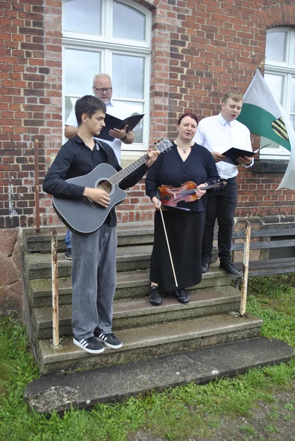 Vier Musiker intonieren ein Volkslied vor dem Empfangsgebäude des Museumsbahnhofs Markersdorf-Taura.