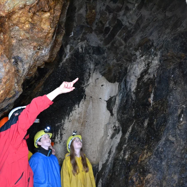 Drei mit bunten Schutzkutten und Schutzhelmen ausgestattete Personen stehen in einem Bergwerksstollen.