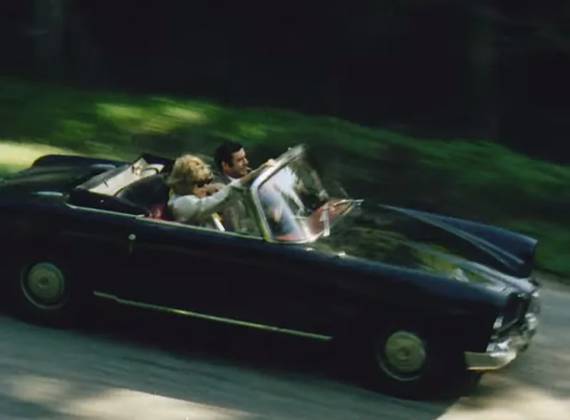 Luftaufnahme eines Mannes und einer Frau in einem fahrenden Cabriolet im Stil der 1960er Jahre