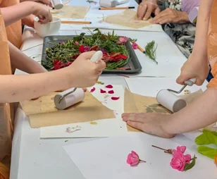Farbgestaltung mit Pflanzen Das Foto zeigt die Hände von Kindern, die sich im Direktfarbdruck mit Pflanzen und Rollen auf einem Papier üben.