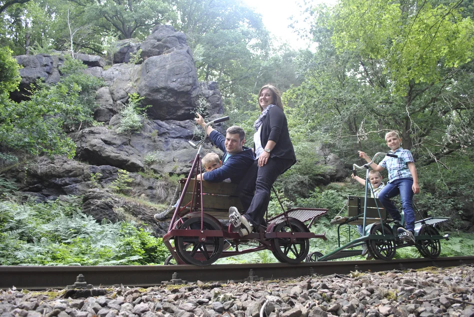 Zwei Fahrrad-Draisinen mit einer Familie fahren auf Schienen unterhalb des Felsmassivs Schreckenstein im Chemnitztal.