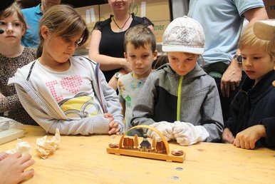 Expothek Mehrere Kinder schauen auf einen kleinen erzgebirgischen Schwibbogen.
