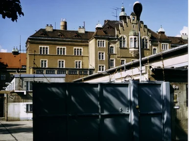Ein halbgeöffnetes Stahltor gibt den Blick frei auf einen Gefängnishof und das dahinter aufragende ehemalige Gefängnisgebäude