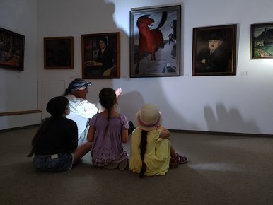 Das Foto zeigt drei Kinder und eine erwachsene Person, die, im Dunkeln auf dem Boden sitzend, mit Taschenlampen Bilder in der Kunstsammlung anleuchten und betrachten.