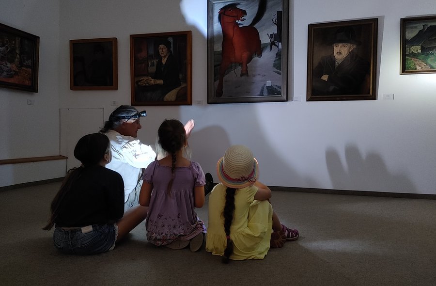 Das Foto zeigt drei Kinder und eine erwachsene Person, die, im Dunkeln auf dem Boden sitzend, mit Taschenlampen Bilder in der Kunstsammlung anleuchten und betrachten.
