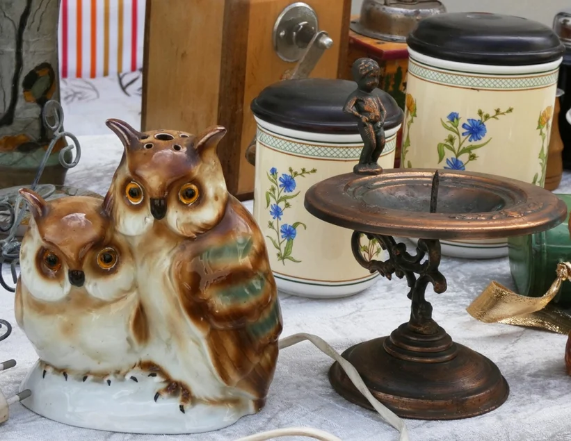 Flohmarktstand Ein Kerzenständer, ein Gewürzstreuer in Eulenform und mehrere Dosen werden auf einem Tisch präsentiert.
