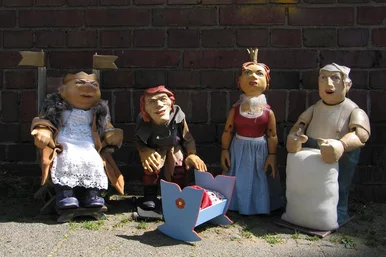 Vier Figurentheaterpuppen stellen einen König, das Rumpelstilzchen, eine Königin und einen Müller dar. Vor den nebeneinander stehenden Figuren steht eine Miniatur-Wiege.