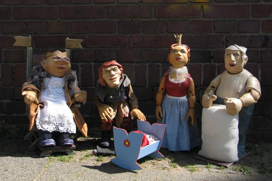 Vier Figurentheaterpuppen stellen einen König, das Rumpelstilzchen, eine Königin und einen Müller dar. Vor den nebeneinander stehenden Figuren steht eine Miniatur-Wiege.