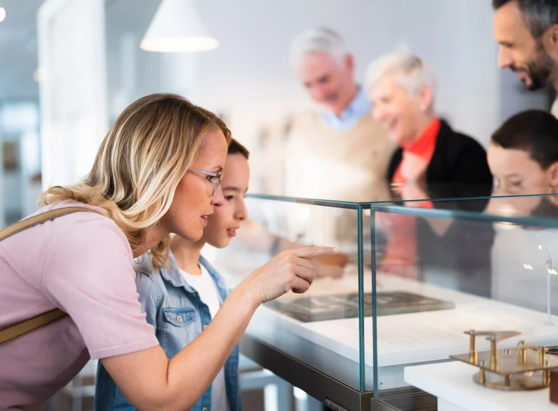 Eine vierköpfige Familie sowie ein älteres Paar schauen interessiert in eine Vitrine mit verschiedenen Exponaten.