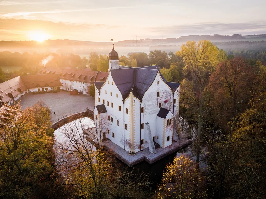 Wasserschloss Klaffenbach Luftbildaufnahme eines kleinen, weiß getünchten, von einem Wassergraben umgebenen Renaissance-Schlosses bei Sonnenuntergang