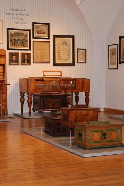 Museumssaal Drei historische Holztruhen und ein historisches Tasteninstrument im Museumssaal, an der Wand hängen diverse Bilder