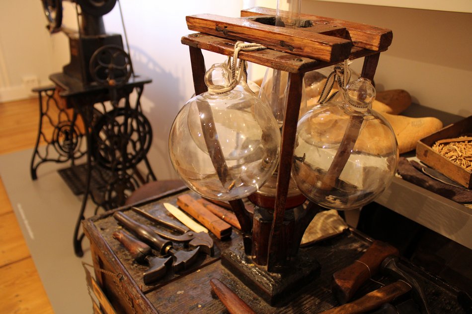 Detailaufnahme einer historischen Werkstattsituation mit diversen Schusterwerkzeigen, im Hintergrund eine alte Nähmaschine