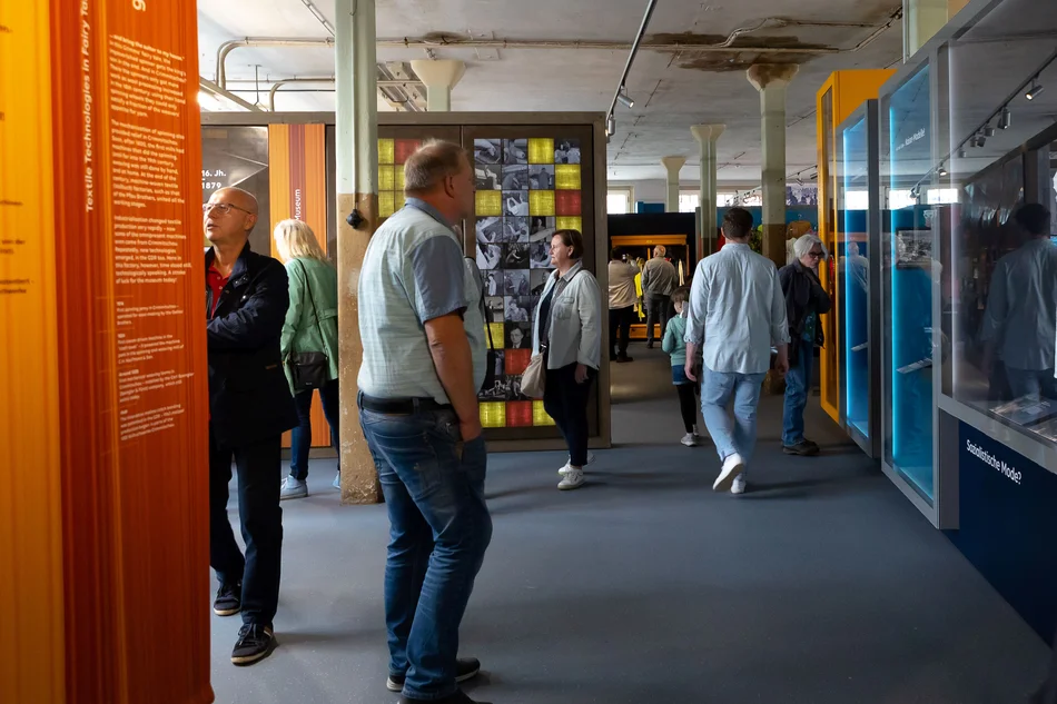 Menschen bewegen sich zwischen Objektvitrinen und Aufstellern mit Ausstellungstexten.