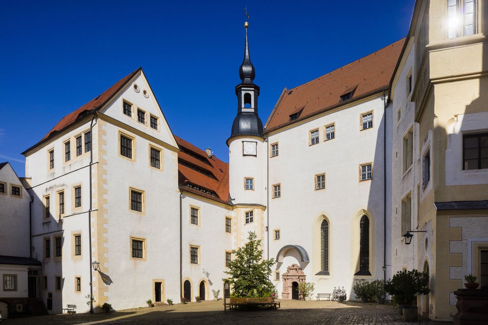 Sommerliche Ansicht des Innenhofes eines großen Schlosses mit weiß getünchter Fassade unter stahlblauem Himmel