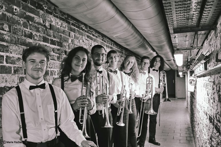 Schwarzweiß-Aufnahme von sieben jungen Musikerinnen und Musikern, die ihre Blasinstrumente in den Händen halten