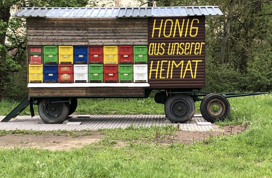 Foto eines Bauwagens in freier Natur, in dem Bienenstöcke installiert sind und der die Aufschrift "Honig aus unserer Heimat" trägt