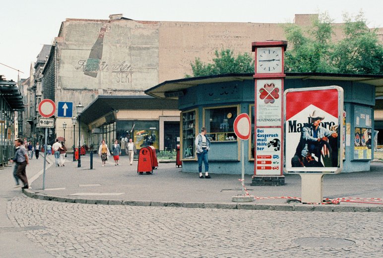 Straßenecke mit einem runden Kiosk, davor eine große Marlboro-Werbung, im Hintergrund verfallende Altbauten