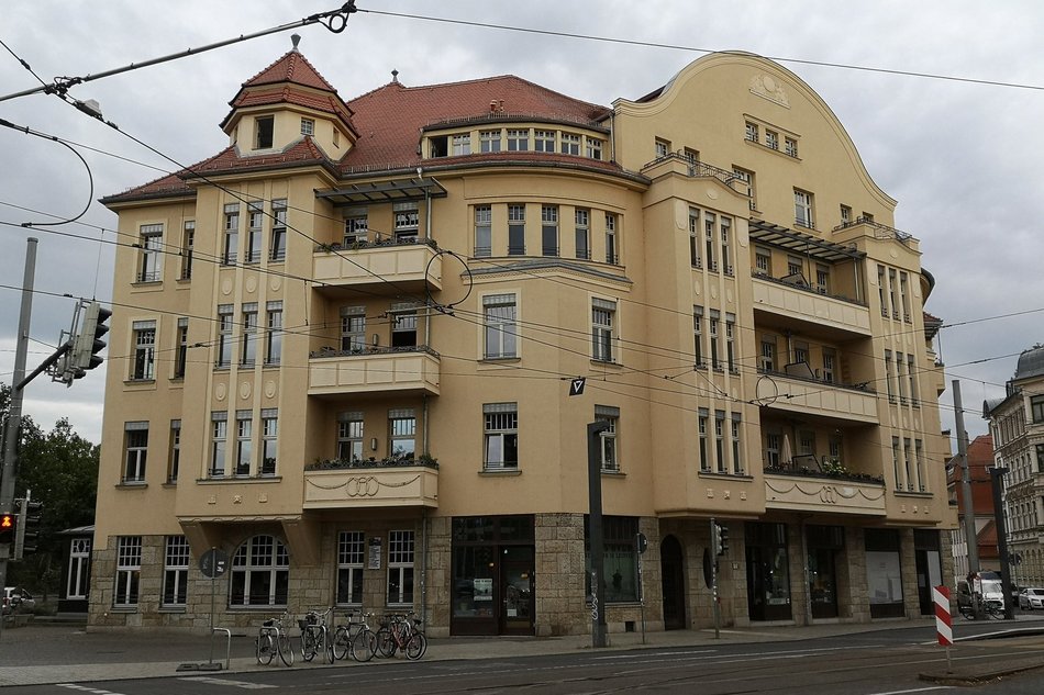 Ein großes, vierstöckiges Eckhaus im Stil der Gründerzeit mit gelber Fassade, Balkonen und einem Türmchen