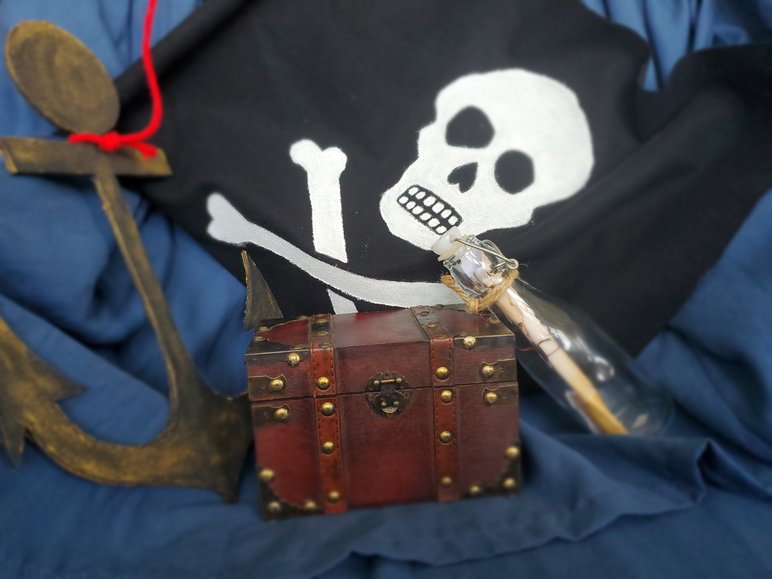 Das Foto zeigt eine Piratenflagge, eine Truhe, eine Flaschenpost und einen Anker.