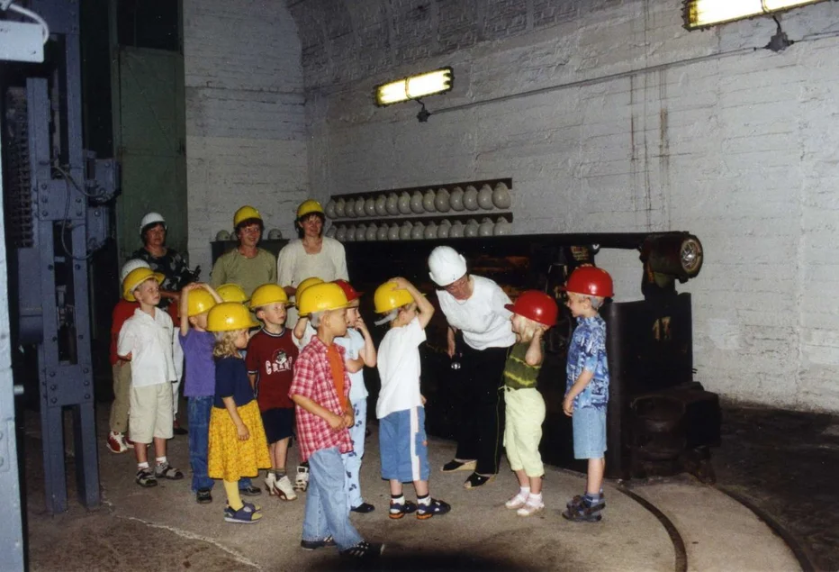 Kinderführung im Bergbaumuseum Eine Kindergruppe und vier Erwachsene stehen in einem authentischen Bereich des ehemaligen Förderturmes. Jede Person trägt einen Schutzhelm.