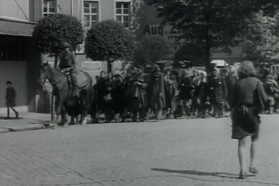 Ungarische Jüdinnen, die von einem Todesmarsch von Leipzig am 25.04.1945 in der Nähe von Wurzen befreit wurden, folgen einem Soldaten Das historisches Schwarzweißfoto zeigt weibliche Häftlinge, die auf einer gepflasterten Straße einem Soldaten auf einem Pferd folgen.