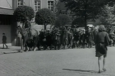 Ungarische Jüdinnen, die von einem Todesmarsch von Leipzig am 25.04.1945 in der Nähe von Wurzen befreit wurden, folgen einem Soldaten Das historisches Schwarzweißfoto zeigt weibliche Häftlinge, die auf einer gepflasterten Straße einem Soldaten auf einem Pferd folgen.
