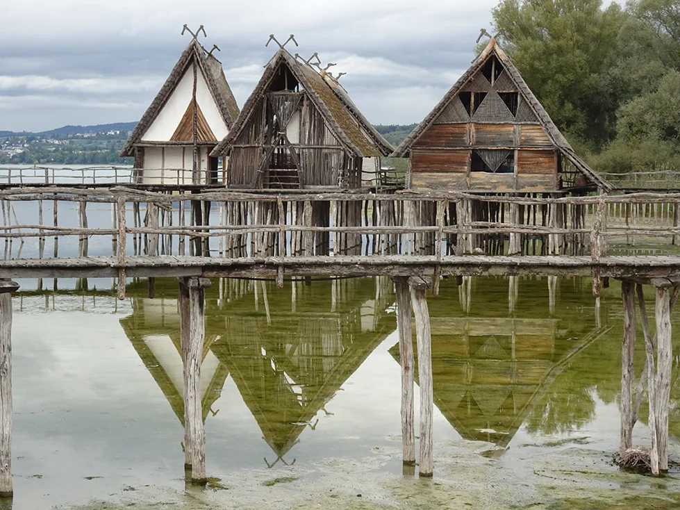 In einem See stehen auf vielen Pfählen errichtet vier Holzhausrekonstruktionen.